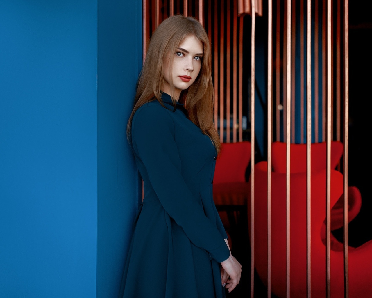 Красивая голубоглазая девушка стоит в пальто у стены