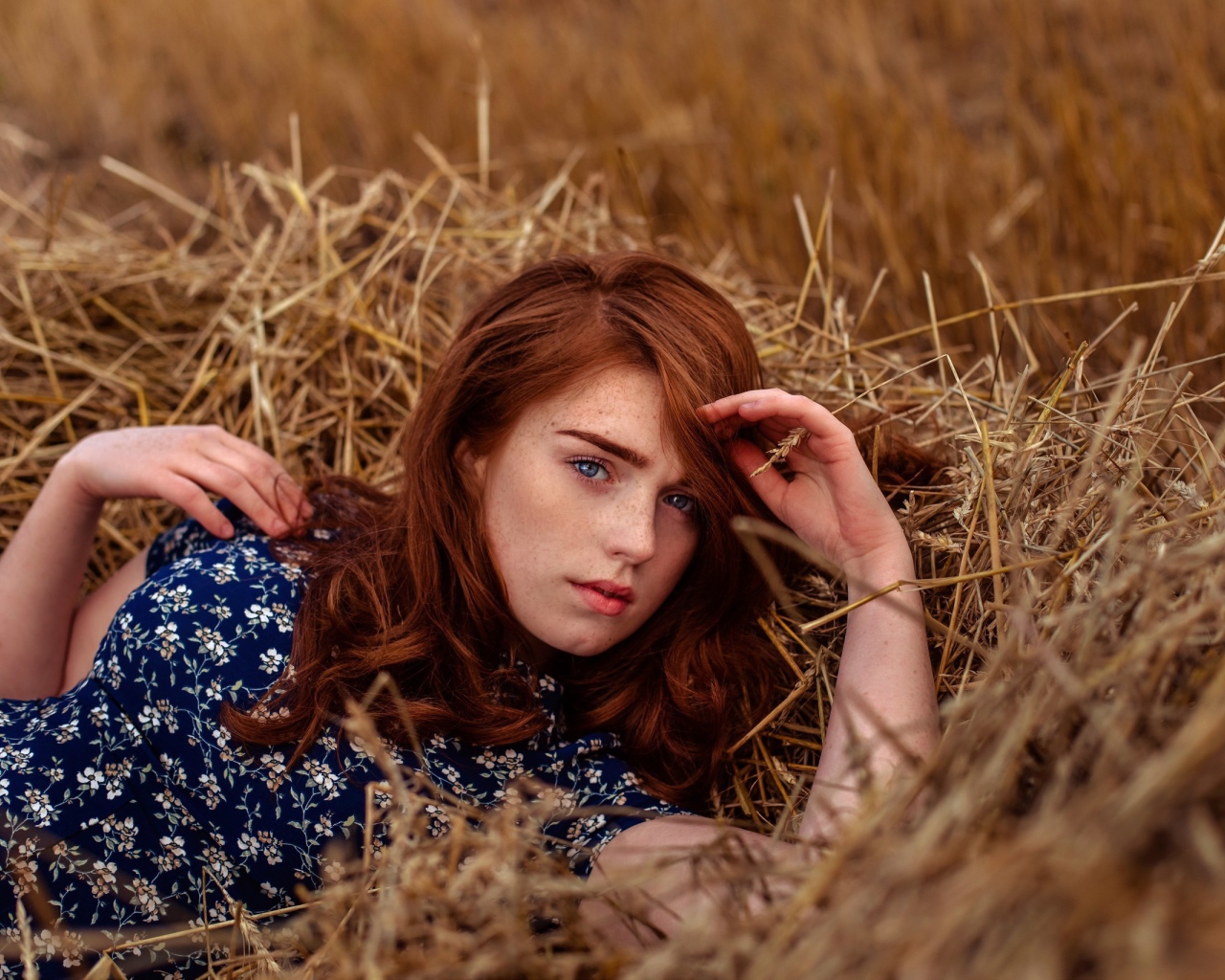 Красивая голубоглазая рыжеволосая девушка лежит в сене