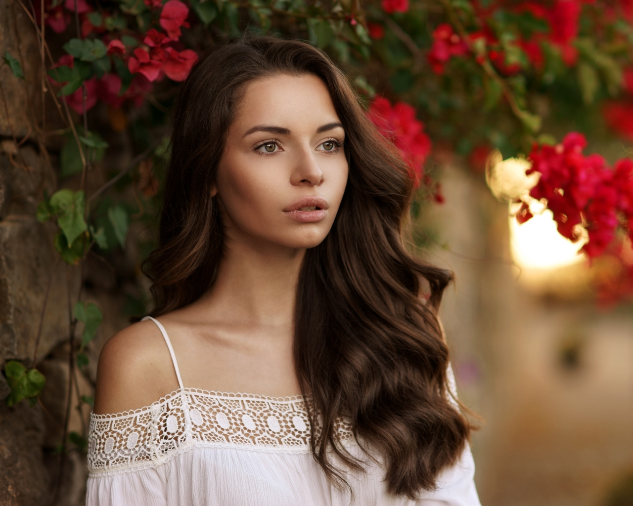 Красивая шатенка у стены на фоне красных цветов