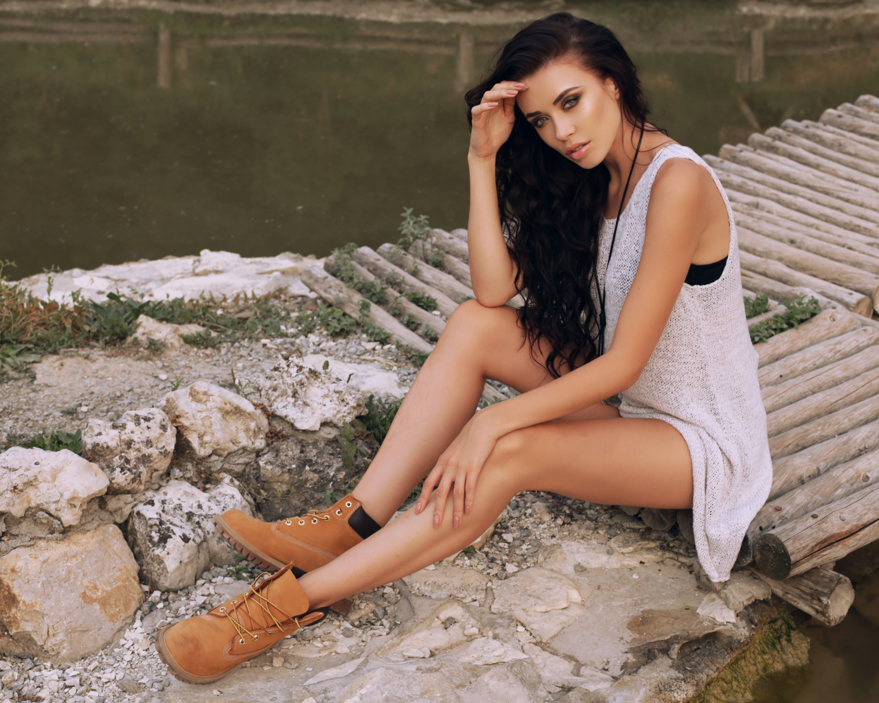 Красивая девушка брюнетка сидит у воды на мостике