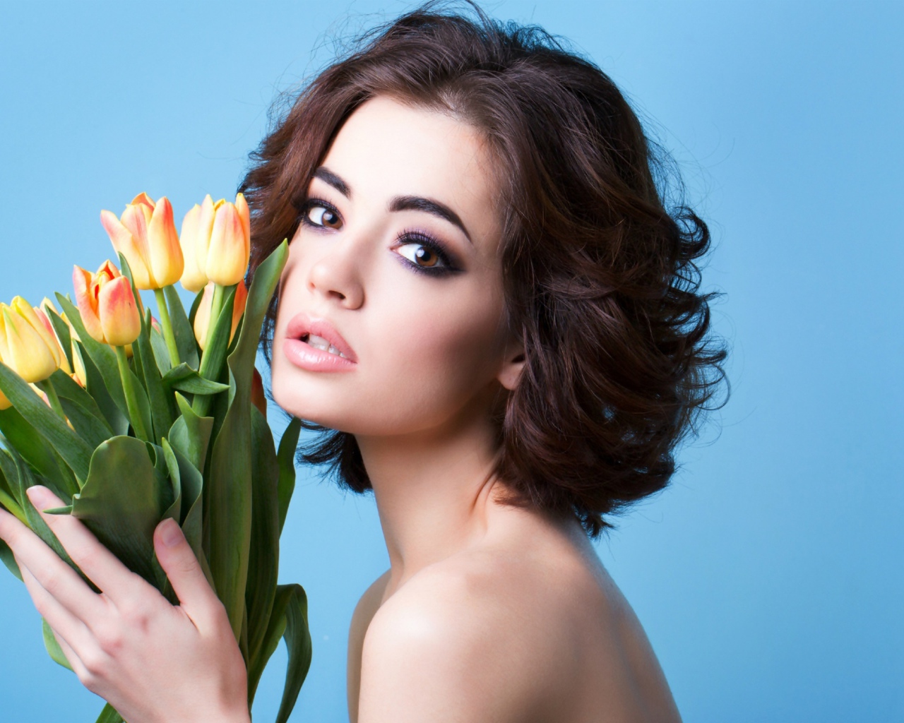 Красивая девушка брюнетка с букетом тюльпанов на голубом фоне