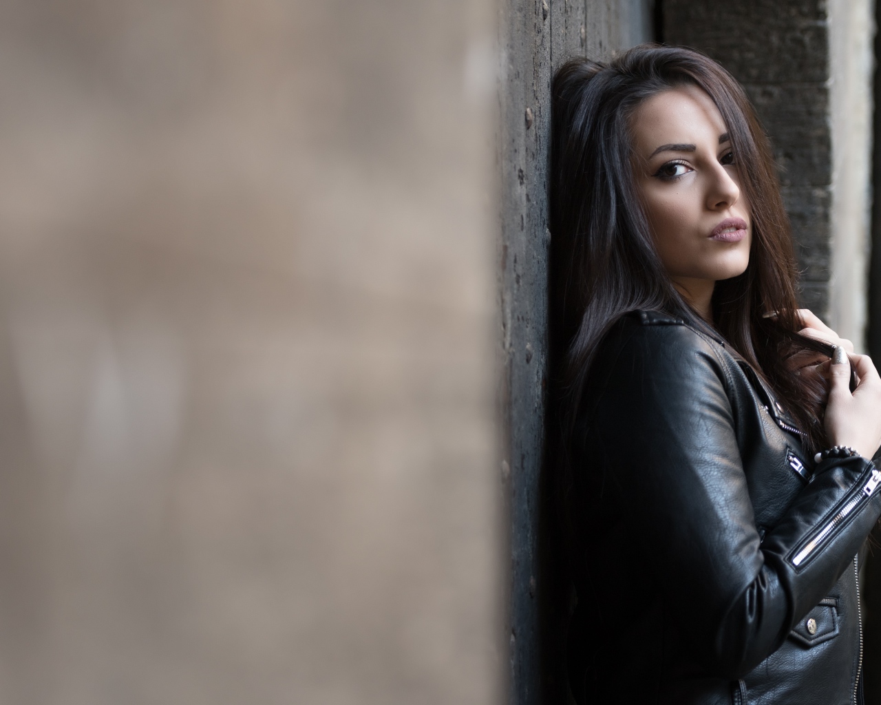 Красивая  брюнетка в кожаной куртке стоит у стены