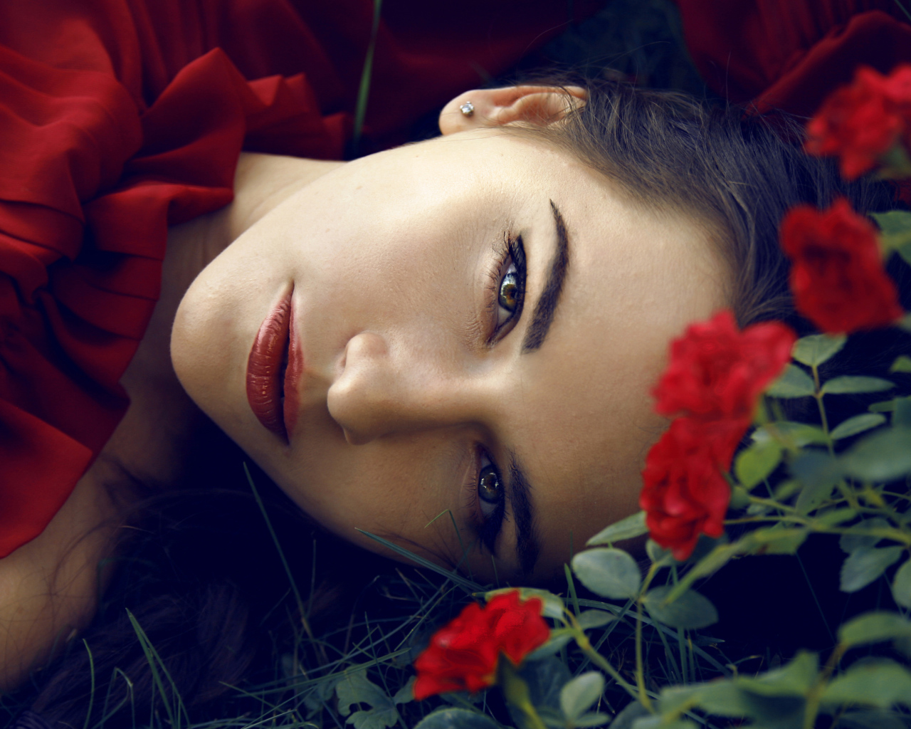 Красивая брюнетка лежит на траве с красными розами