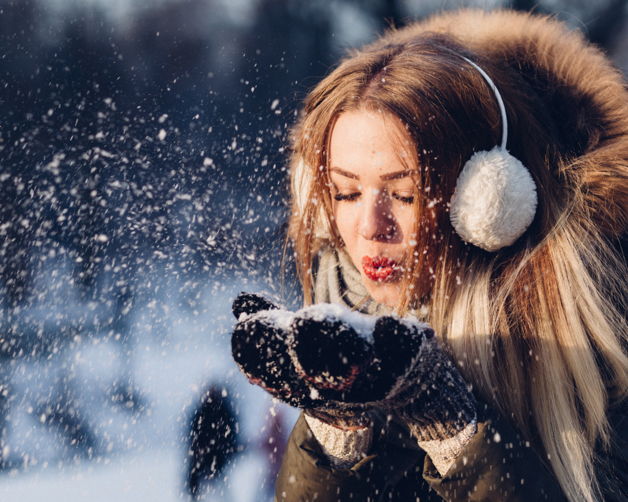 Красивая девушка сдувает снег с ладоней зимой