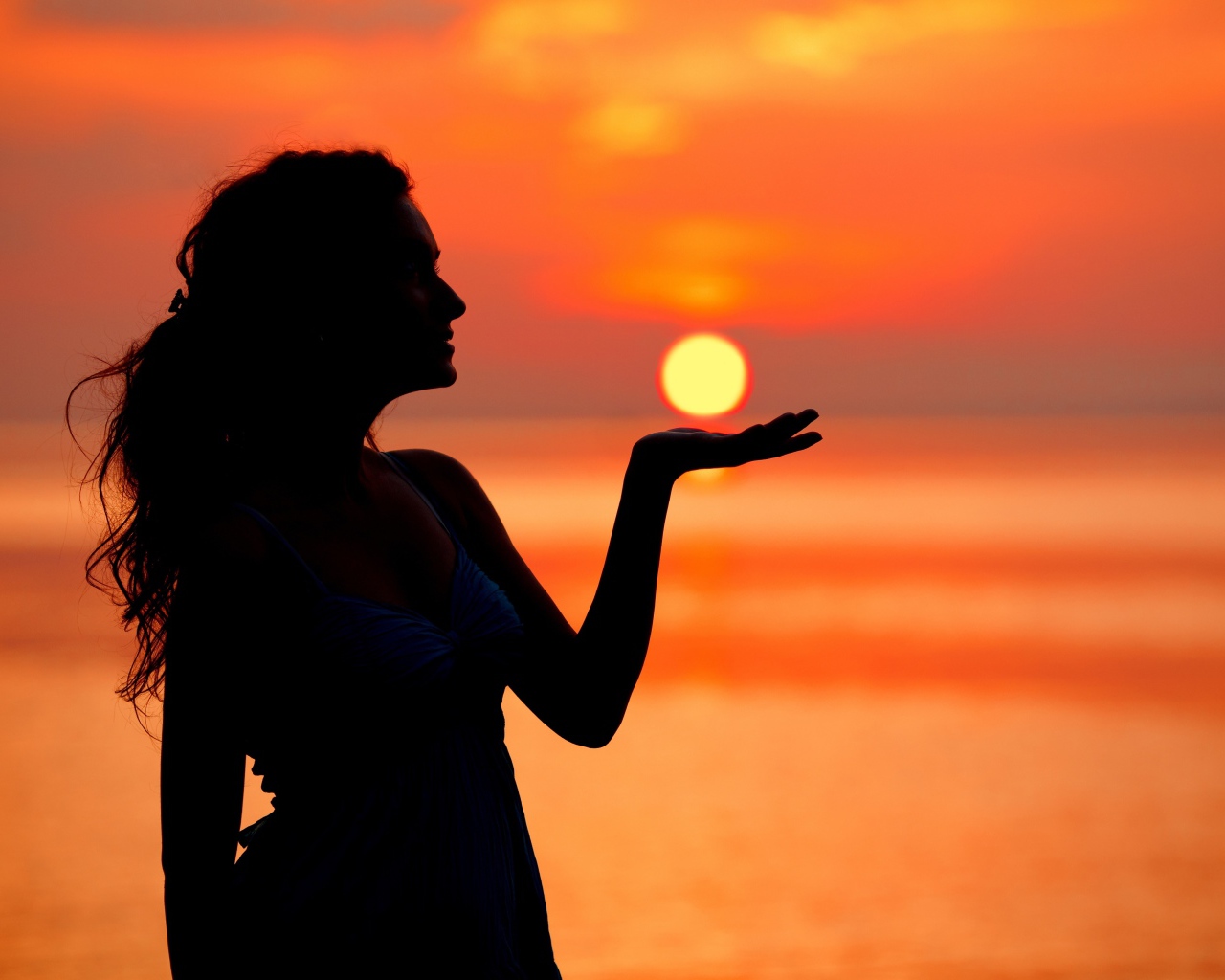 Красивая девушка держит солнце в ладони на закате