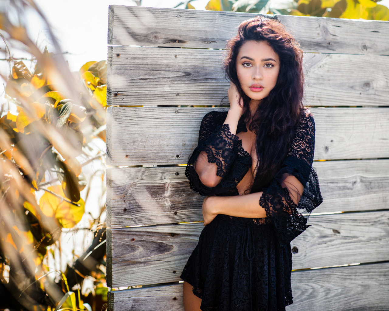 Красивая девушка в черном платье у стены 