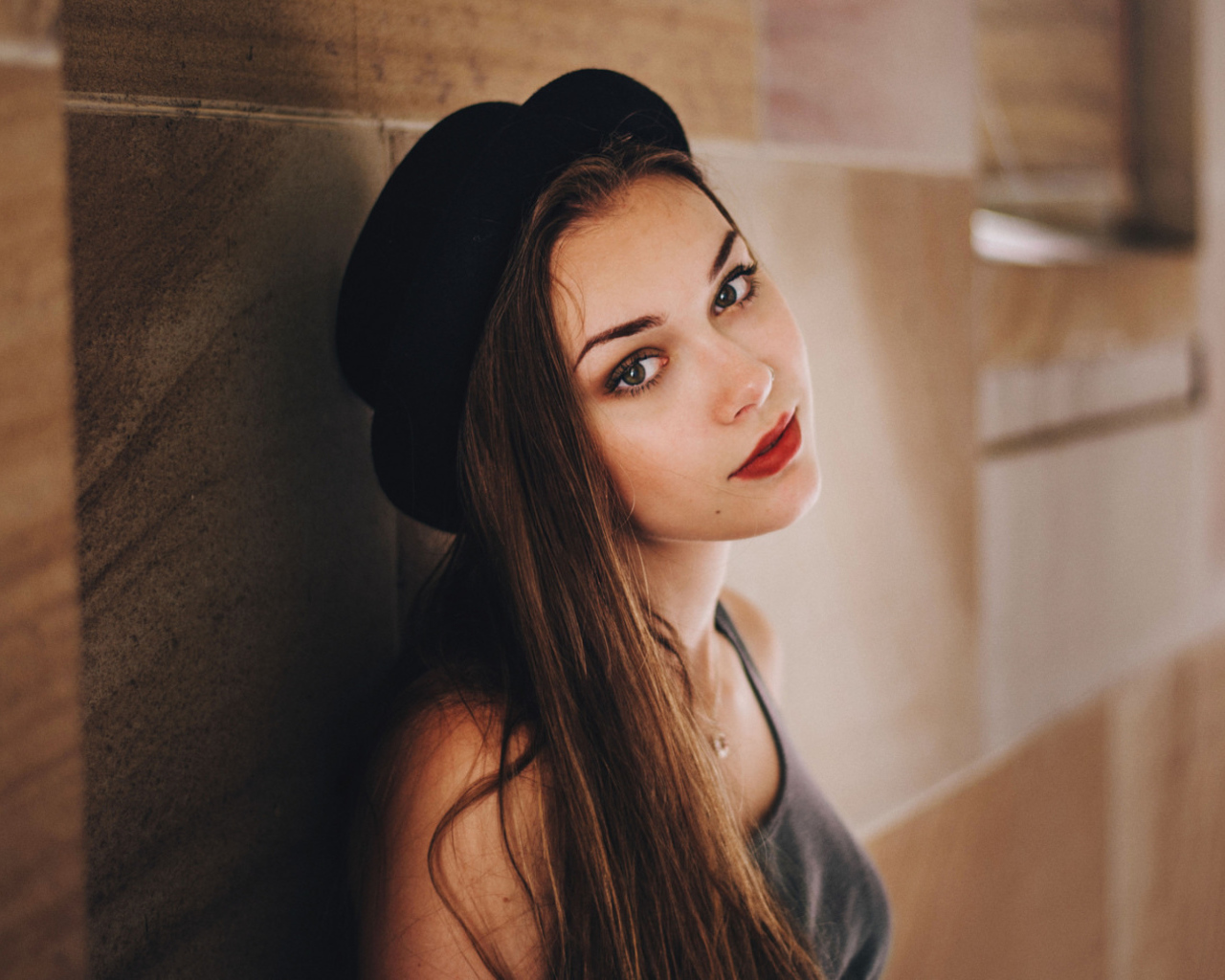 Красивая девушка в черной шляпе у стены 