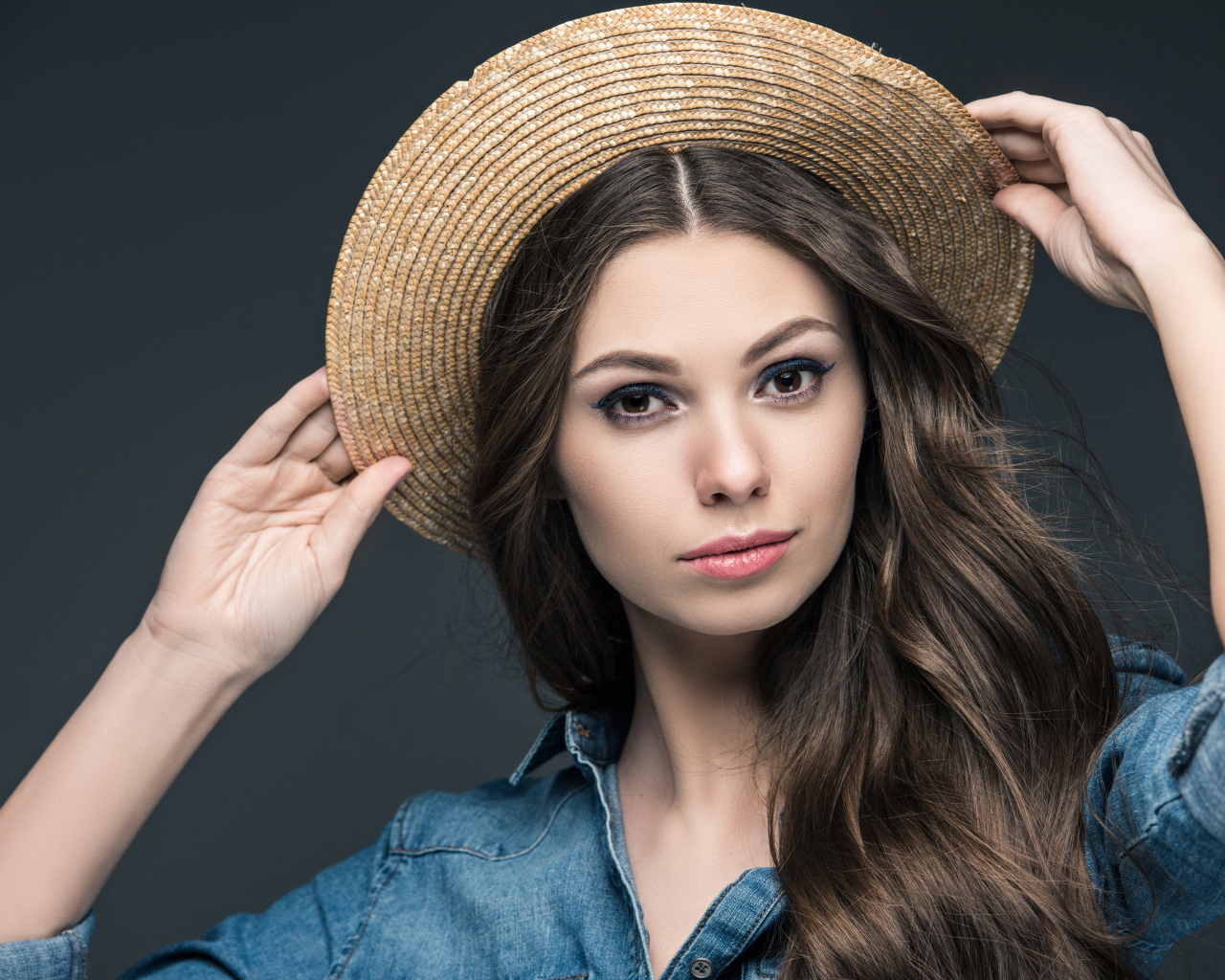 Красивая девушка в соломенной шляпе на сером фоне