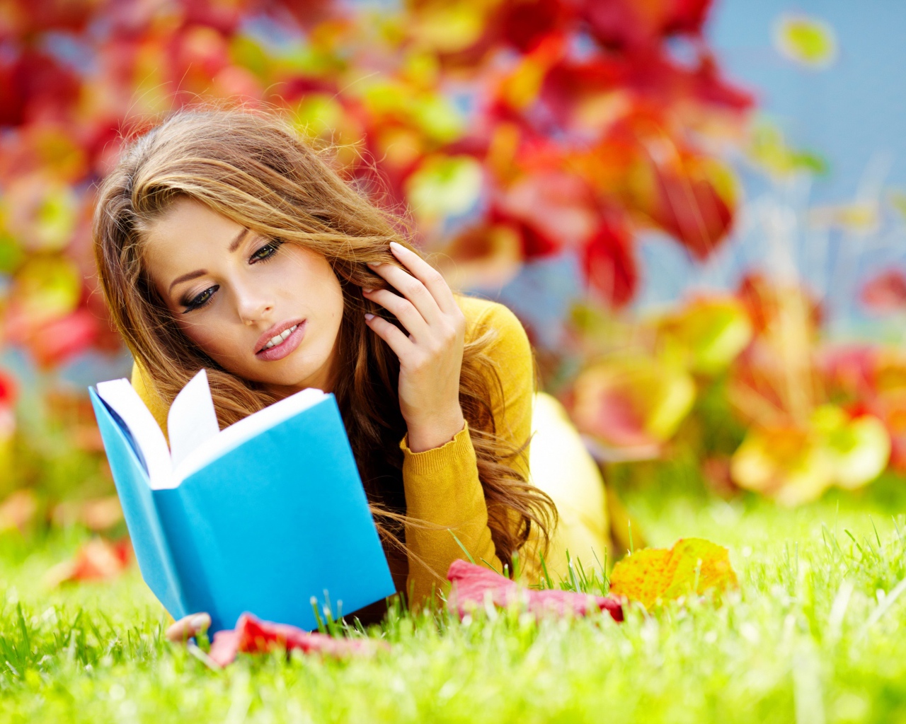 Красивая девушка читает книгу лежа на зеленой траве