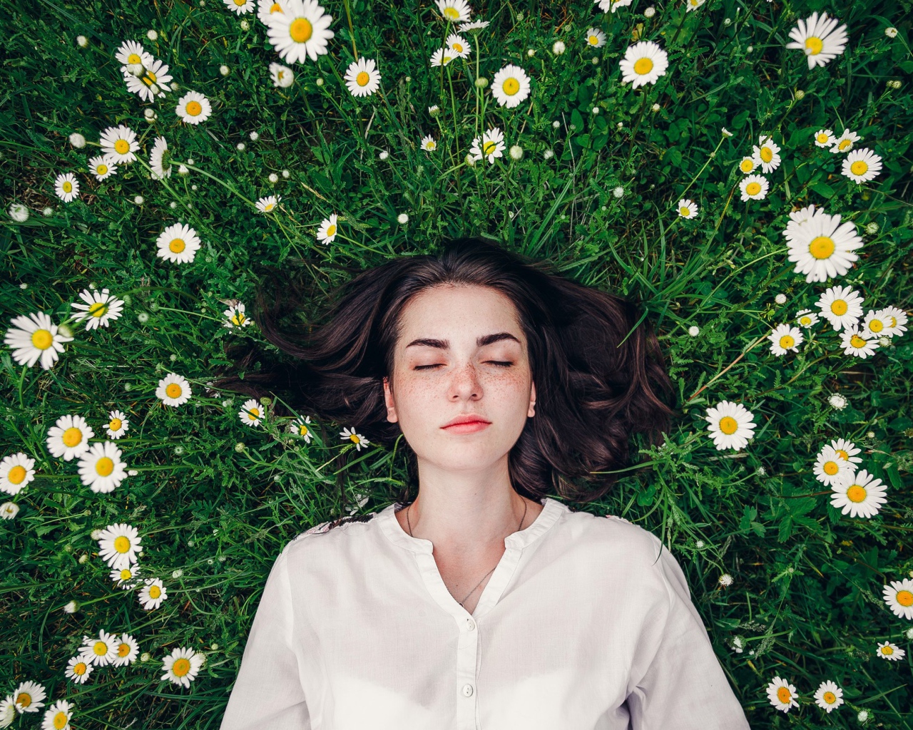 Красивая девушка лежит на зеленой траве с ромашками