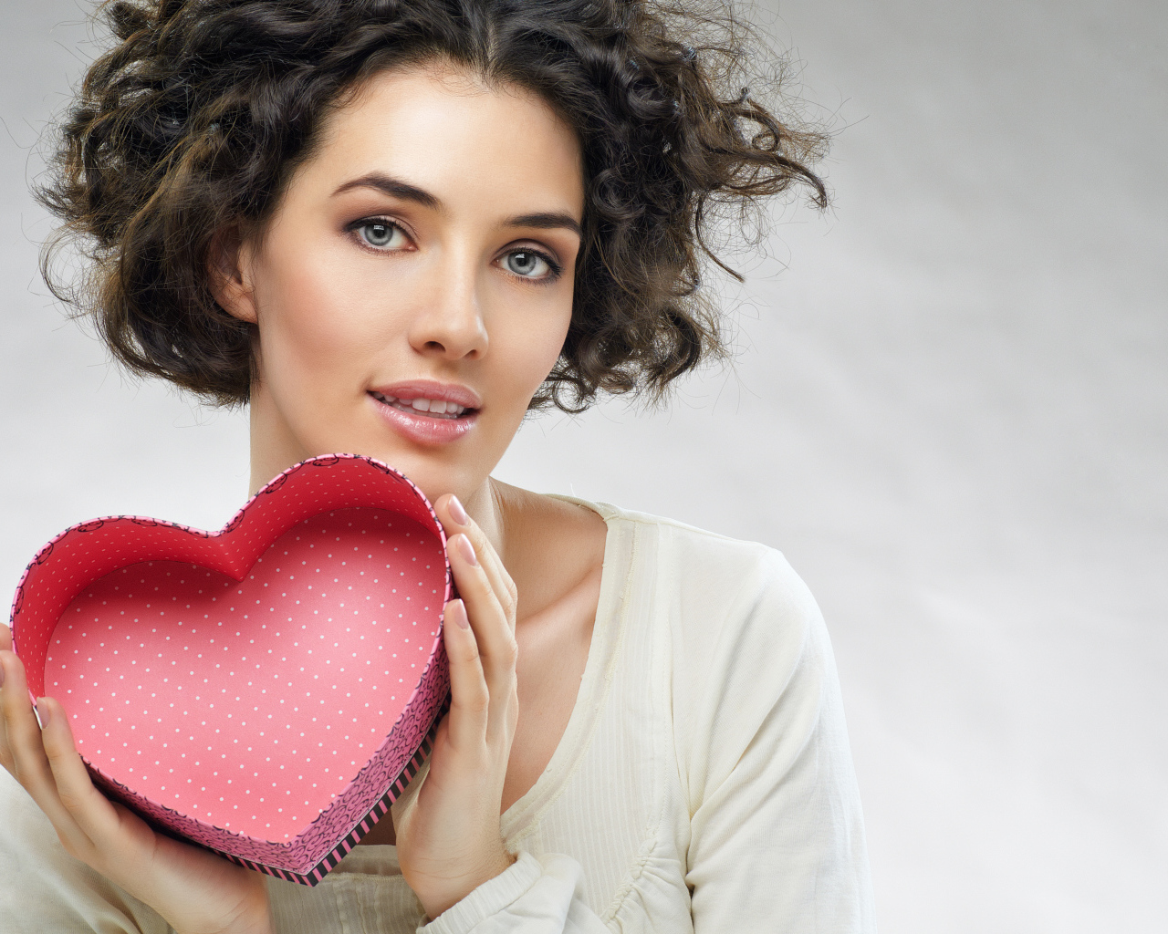 Красивая девушка с коробкой в форме сердца в руках на сером фоне