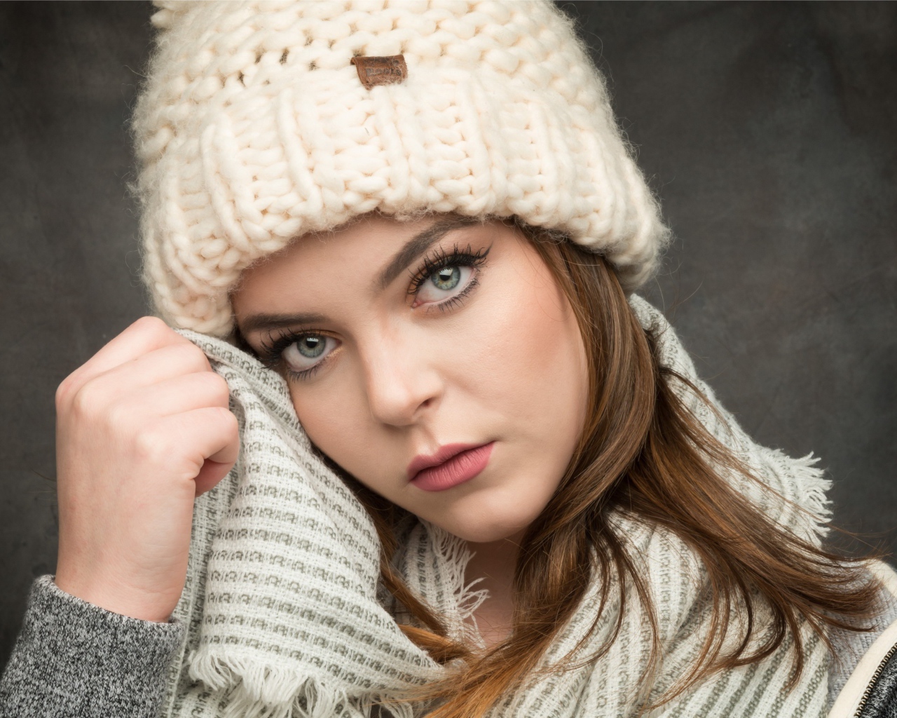 Красивая зеленоглазая девушка в белой вязаной шапке с шарфом