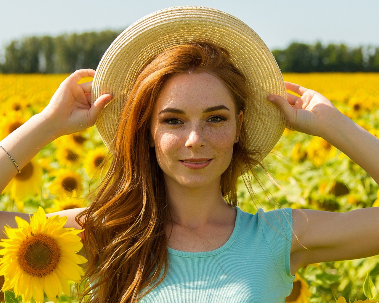 Красивая рыжеволосая девушка в шляпе на поле с подсолнухами 