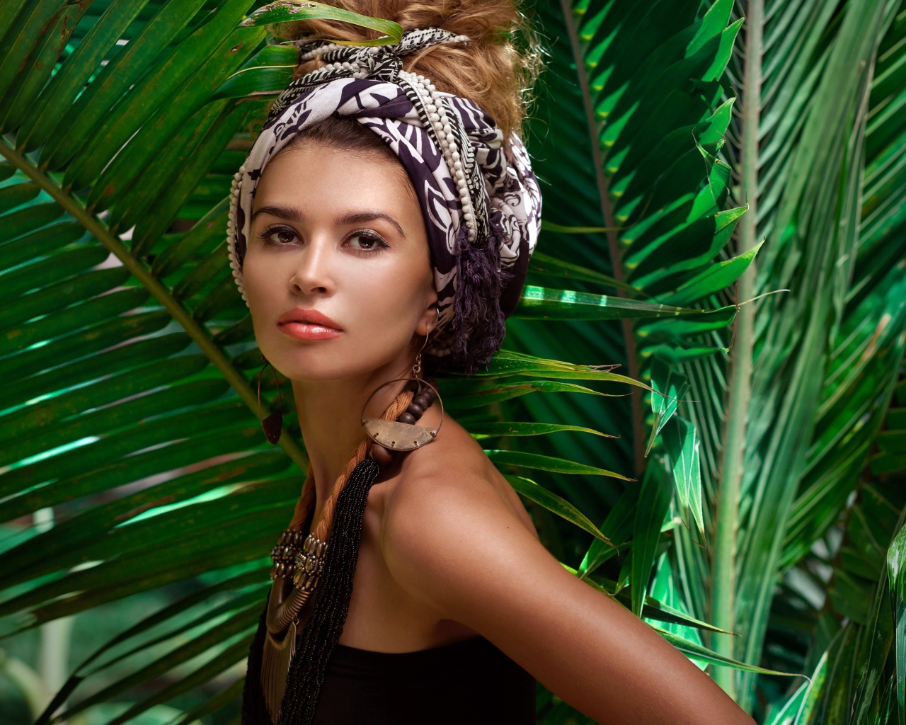 Красивая женщина в тюрбане с украшениями среди зеленых пальмовых листьев
