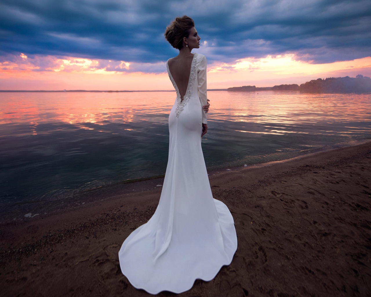 Красивая молодая девушка в свадебном платье у воды на закате 