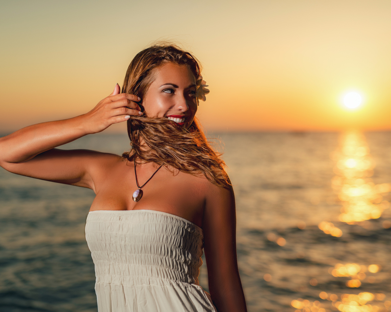 Очаровательная улыбающаяся девушка шатенка на берегу моря на закате