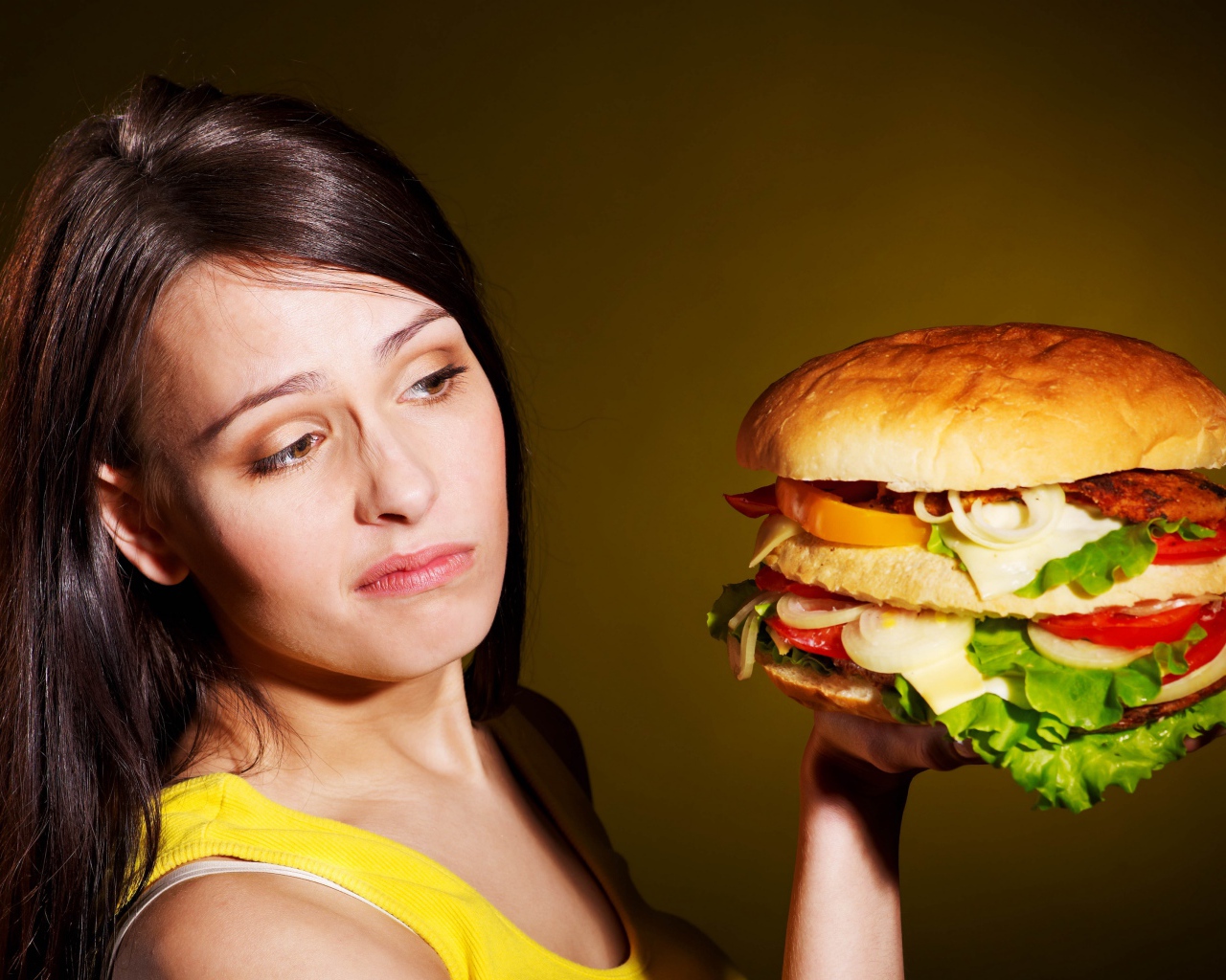 Недовольная девушка с большим гамбургером в руках 