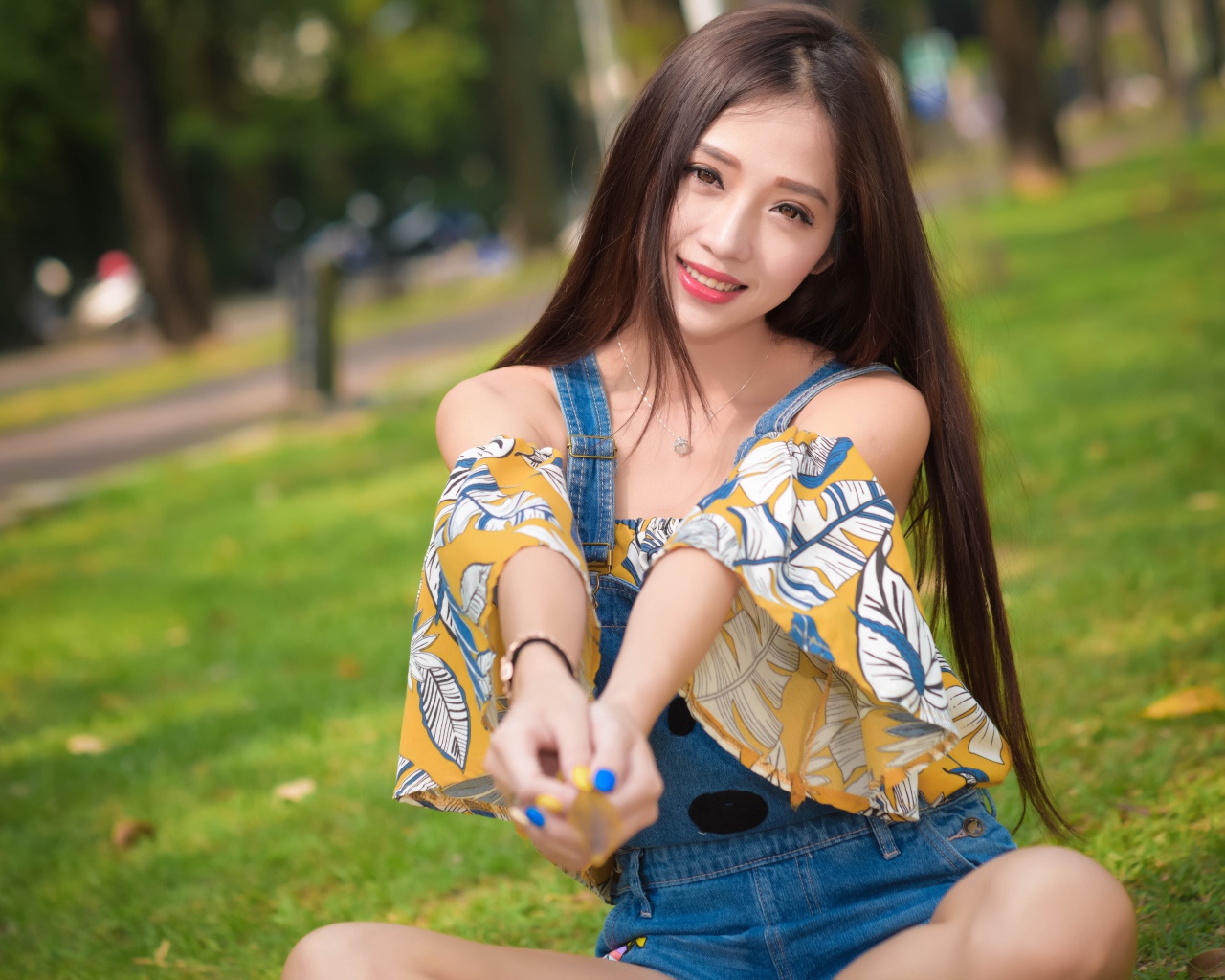 Улыбающаяся девушка азиатка сидит на траве