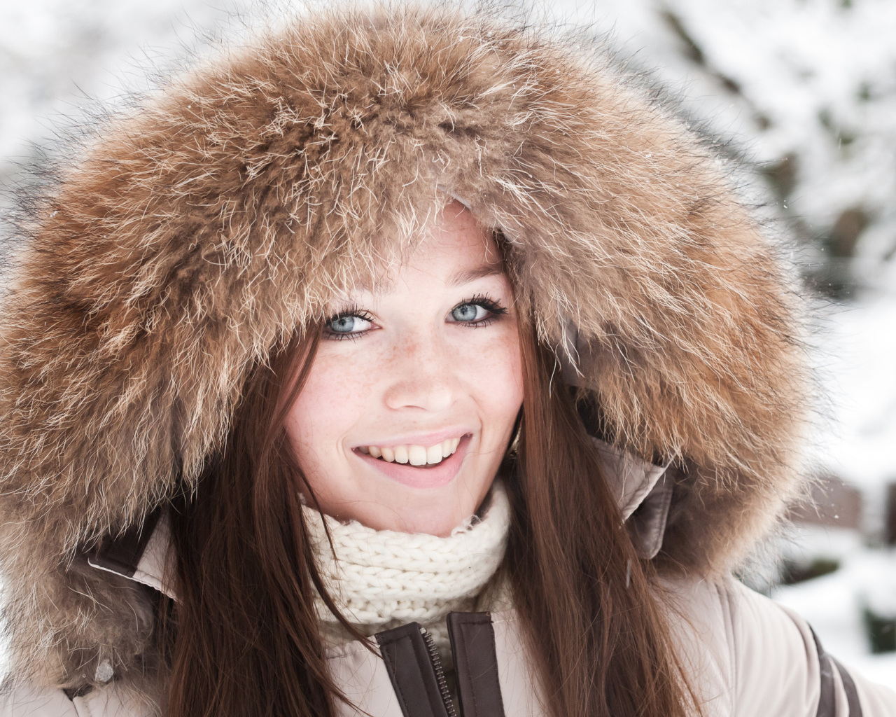 Улыбающаяся голубоглазая девушка в капюшоне зимой