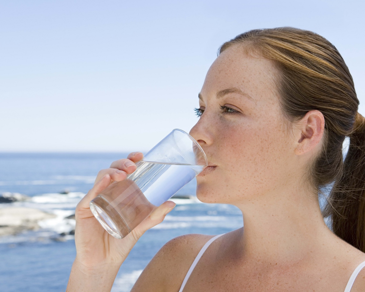 Девушка пьет воду со стакана на фоне моря