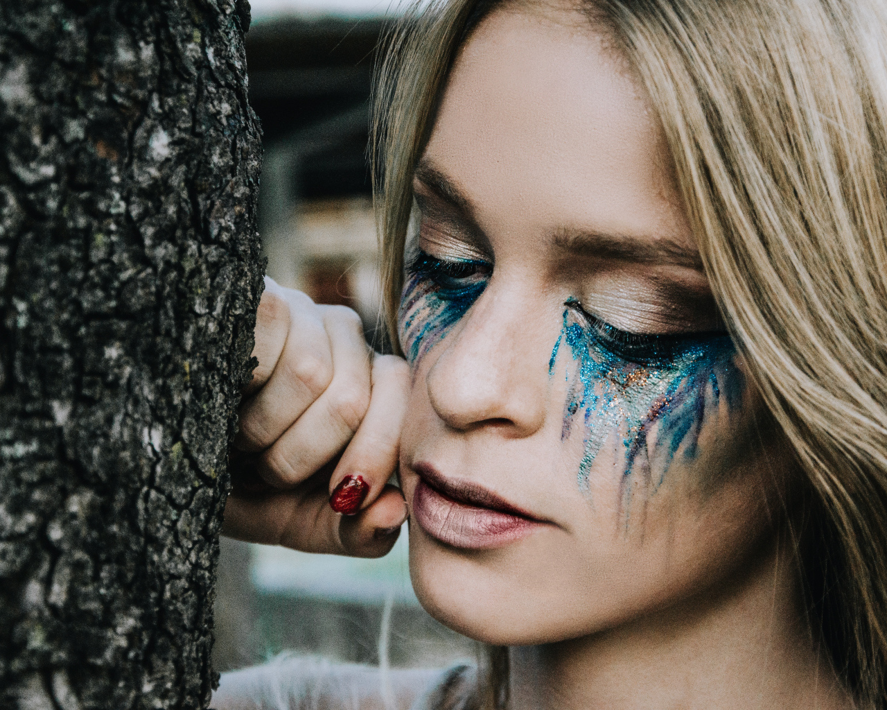 Заплаканная блондинка стоит у дерева