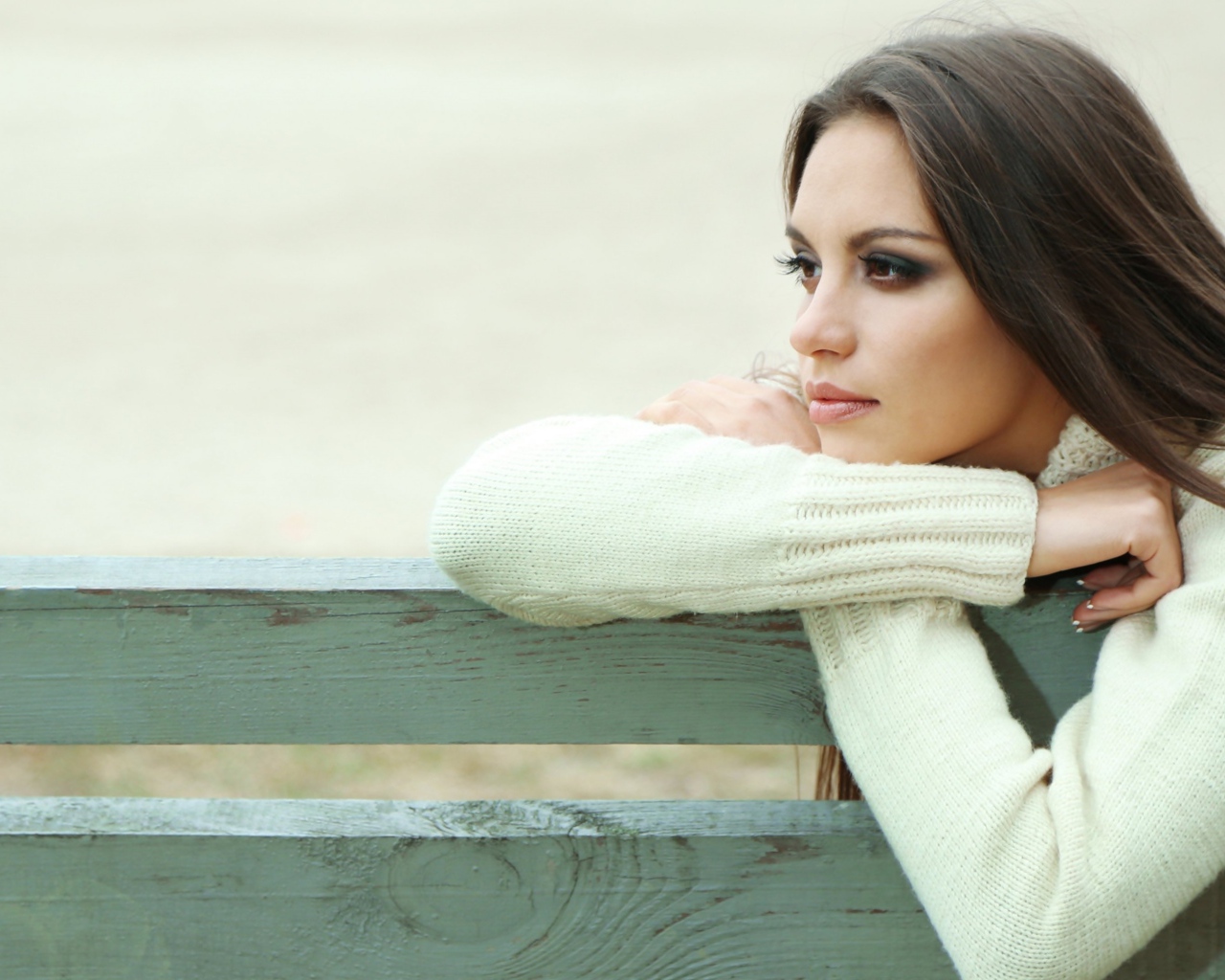 Задумчивая девушка брюнетка в белом свитере сидит на лавке