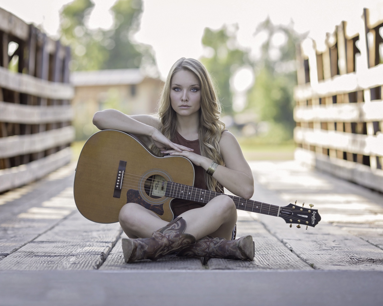 Молодая девушка блондинка сидит на мосту с гитарой