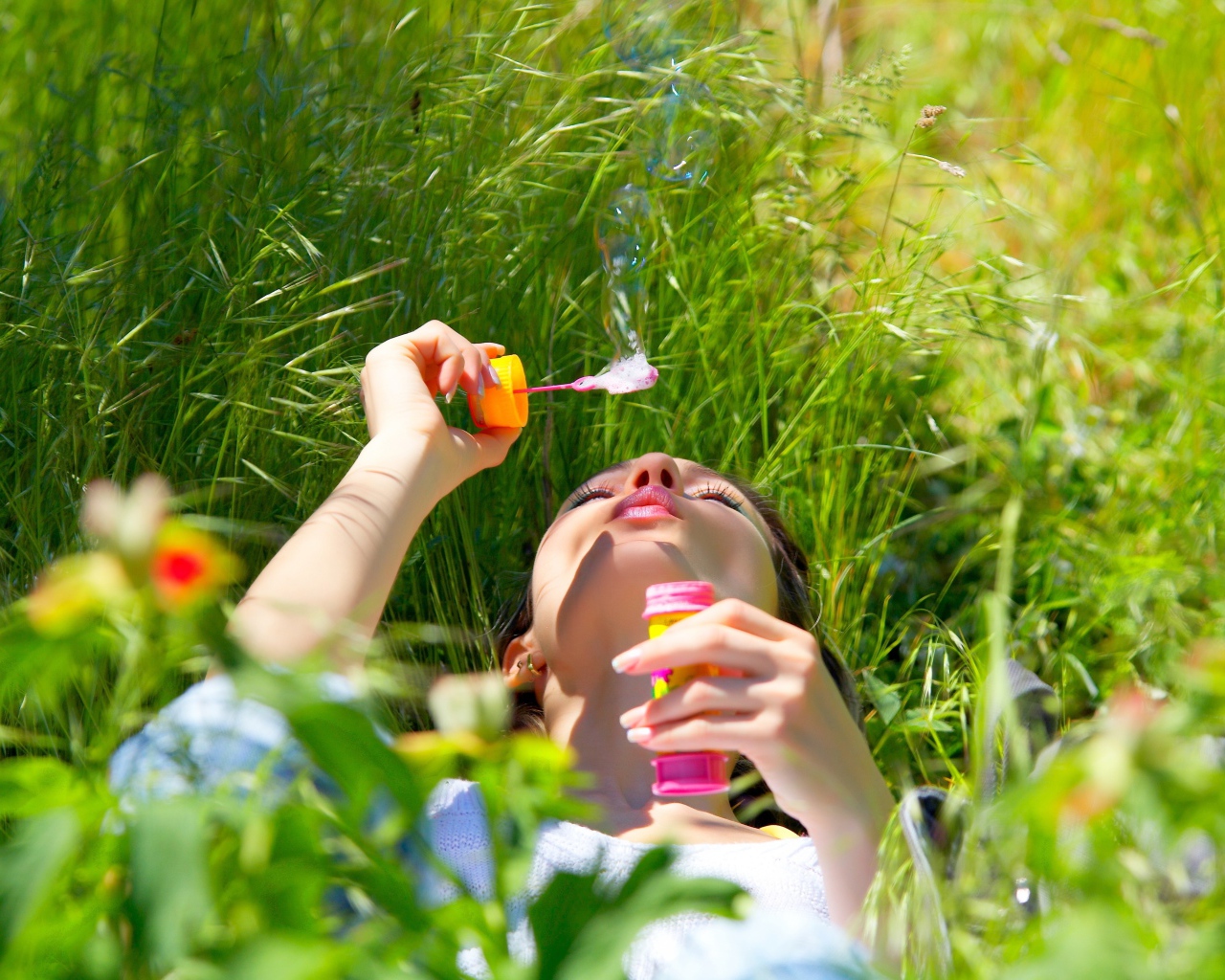 Молодая девушка лежит на зеленой траве с мыльными пузырями