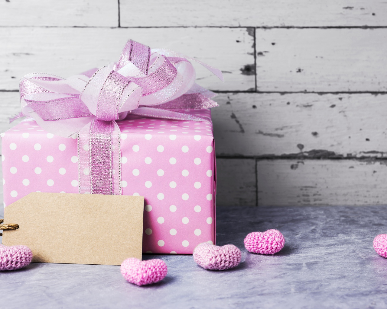 Большая сиреневая подарочная коробка с бантом и маленькими сердечками на фоне стены