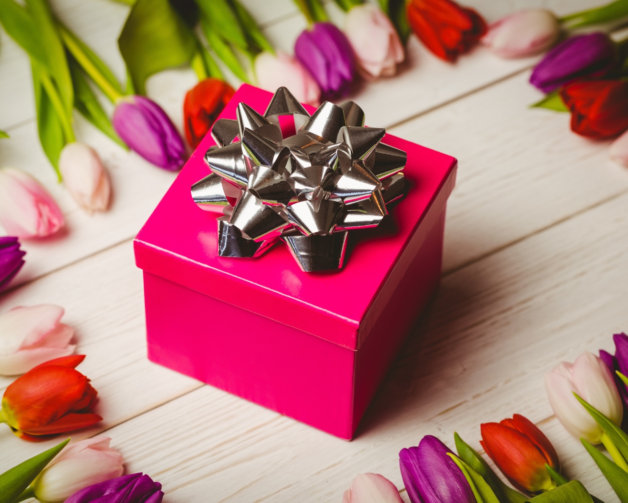 Красная коробка с подарком на столе с тюльпанами