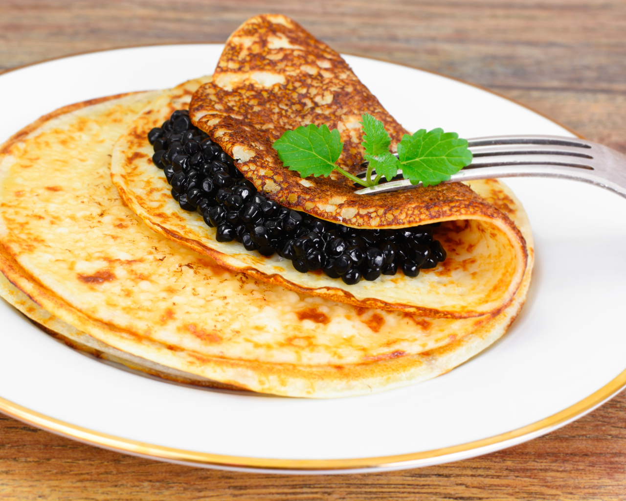 Блины с черной икрой на тарелке с вилкой