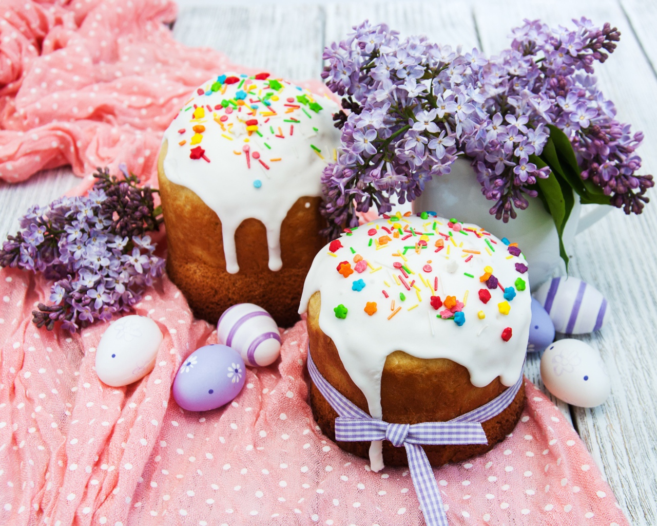 Пасхальные куличи с сахарной глазурью на столе с крашеными яйцами и букетом сирени на Пасху