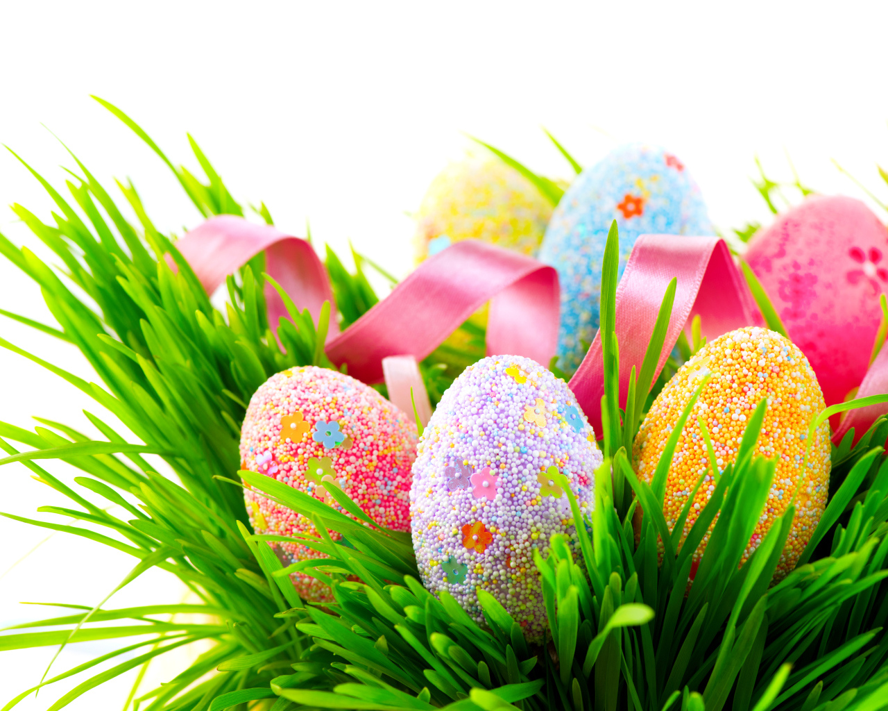 Пасхальные яйца в зеленой траве с розовой лентой на белом фоне
