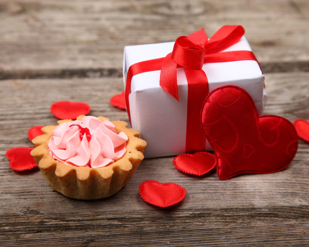 Подарок с красными сердечками и пирожным на столе