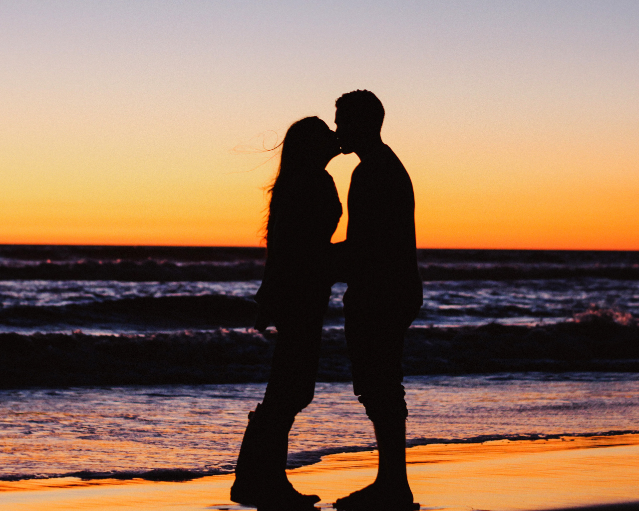 Поцелуй влюбленной пары на берегу моря на закате 
