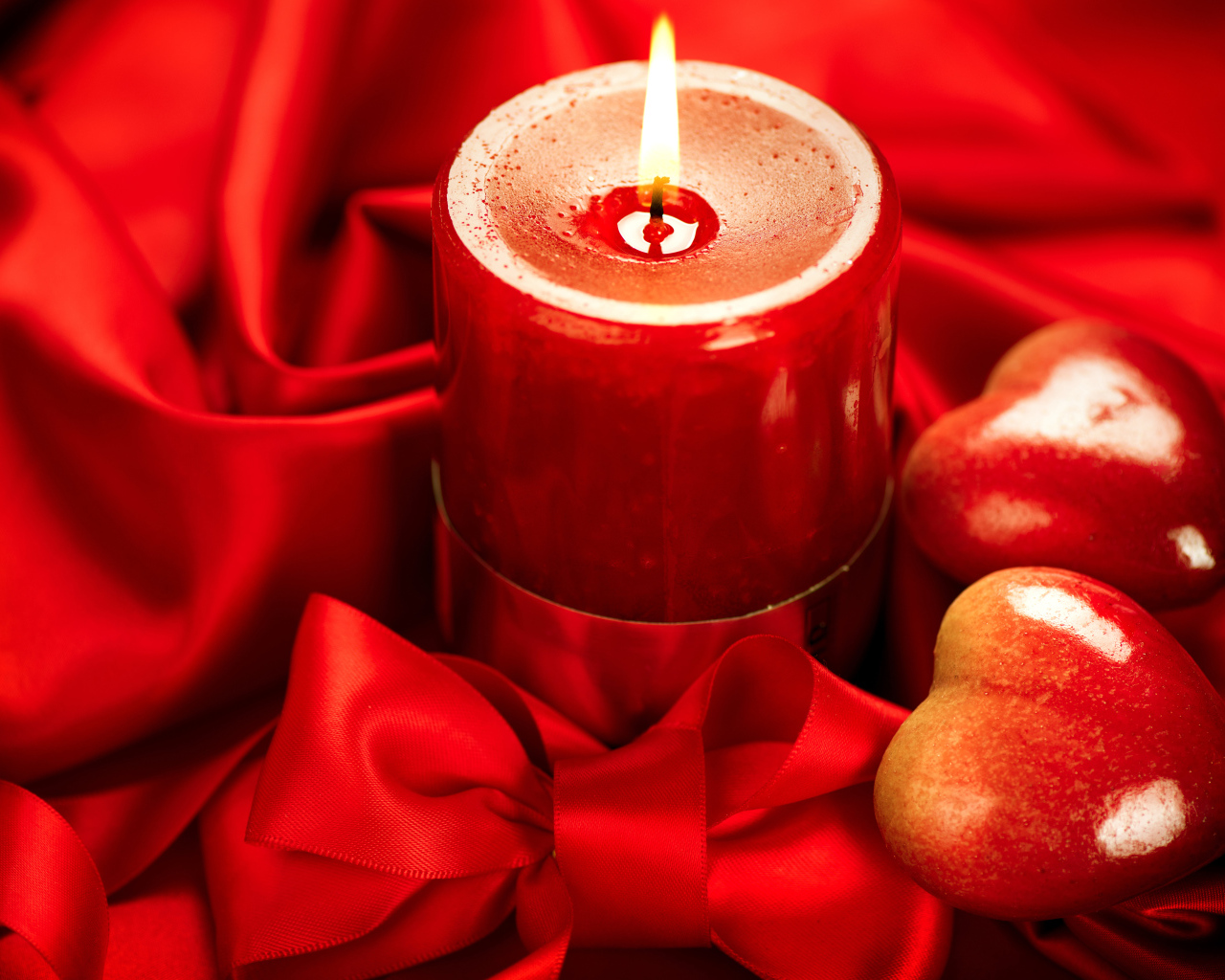 Зажженная свеча с двумя сердечками на красном фоне с бантом