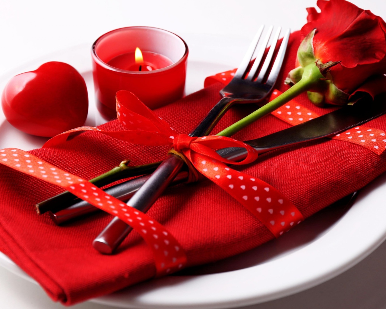 Роза, столовые приборы и зажженная свеча на белой тарелке 