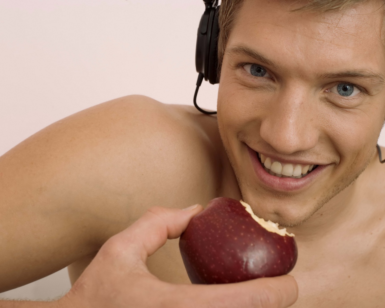 Красивый голубоглазый парень в наушниках с яблоком в руке