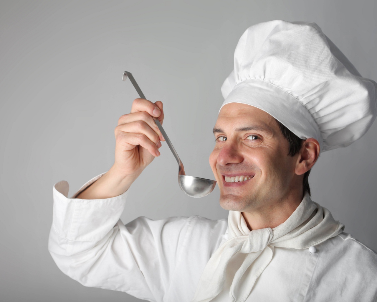 Улыбающийся мужчина повар с половником в руках на сером фоне
