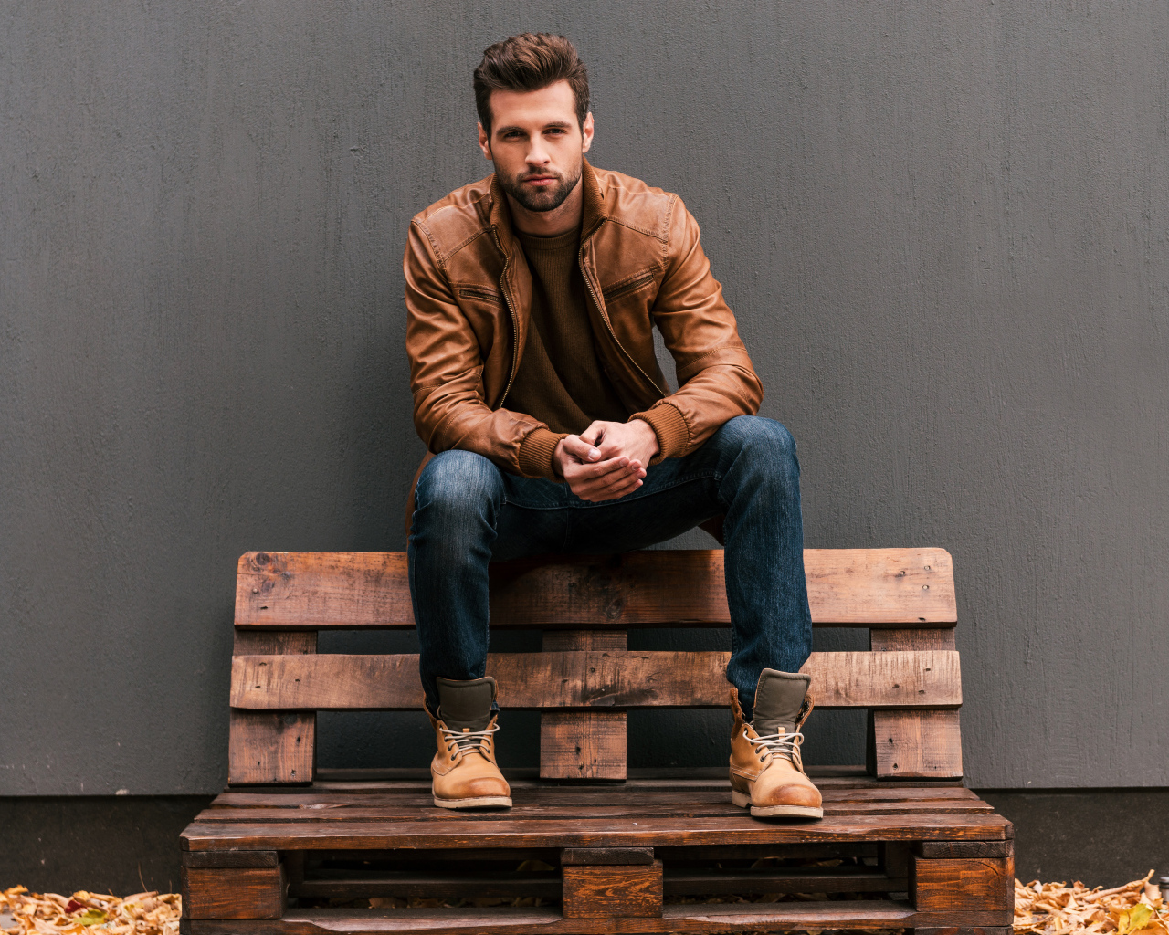 Молодой красивый мужчина сидит на деревянной лавке