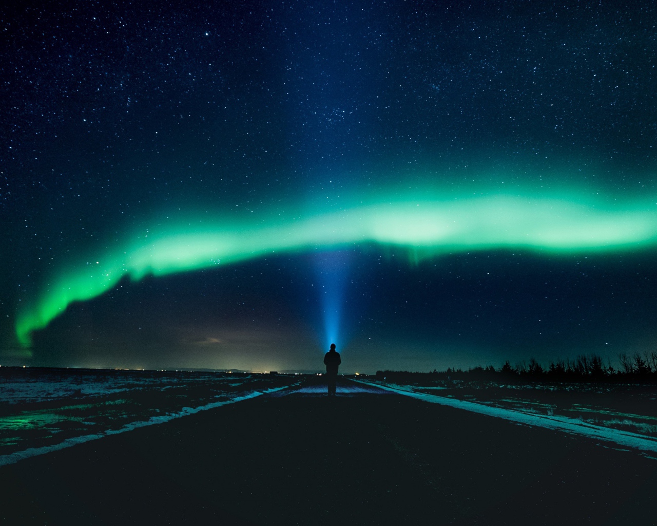 Человек идет по дороге ночью на фоне северного сияния
