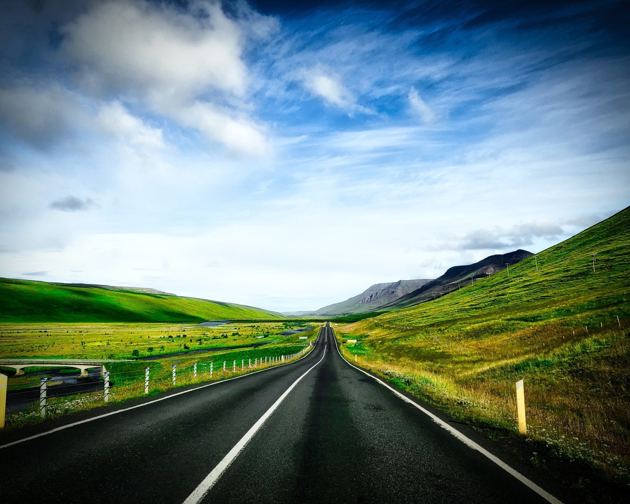 Ровная дорога у зеленых холмов на фоне голубого неба