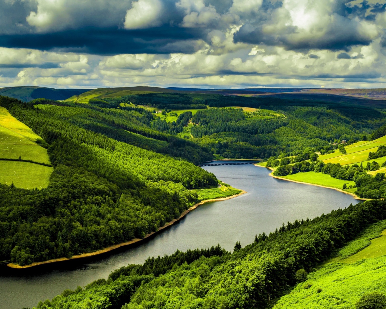 Зеленые холмы у реки под небом с густыми белыми облаками