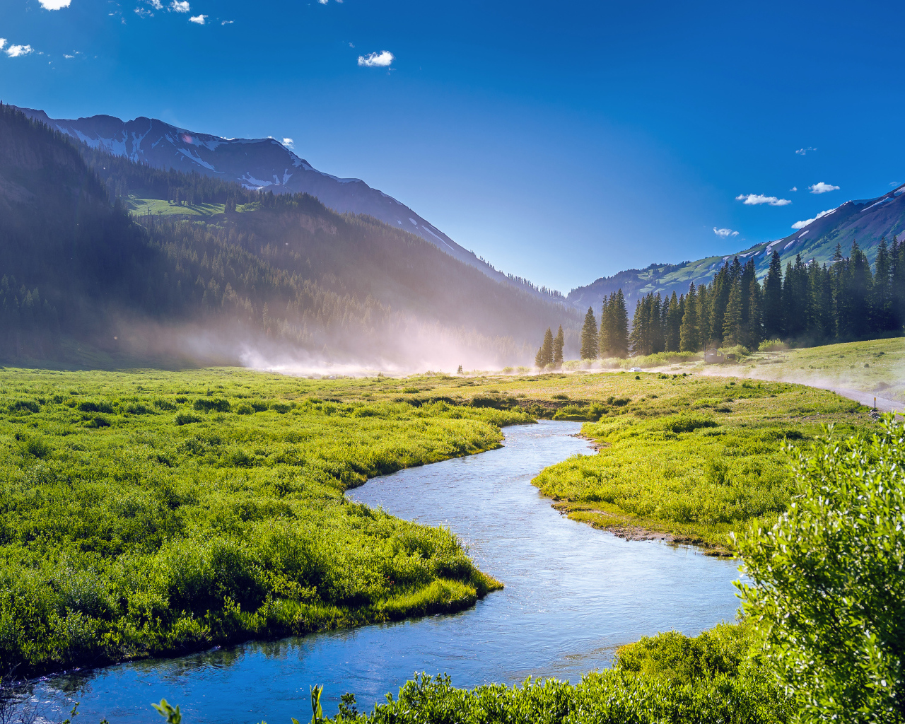 Речка на фоне покрытых зеленью гор под голубым небом