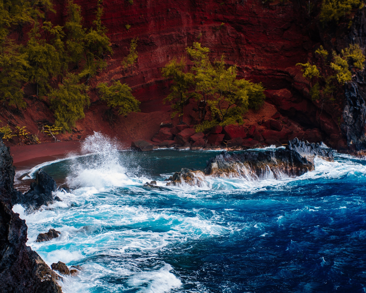 Грубое море брызгает камнями перед красным песчаным океанским заливом в Хане