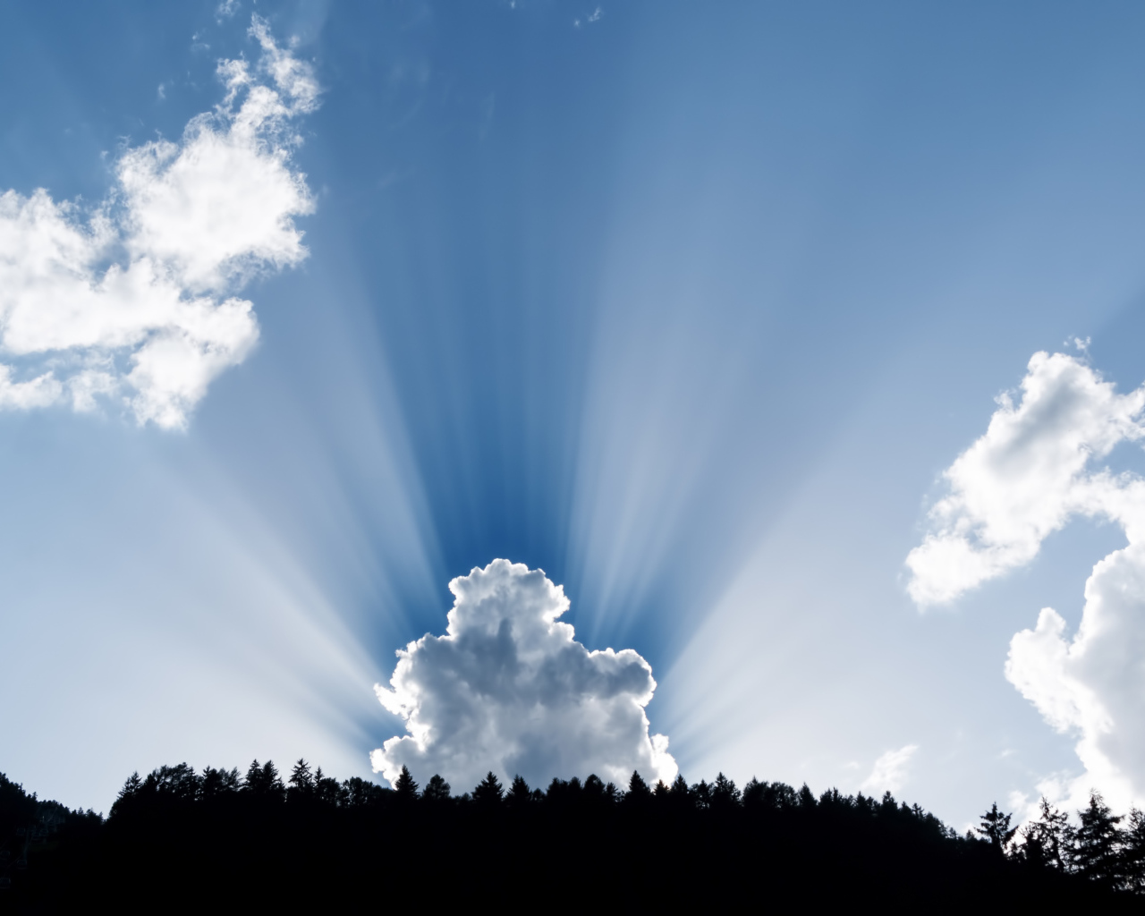 Лучи солнца пробиваются сквозь белые облака в голубом небе 