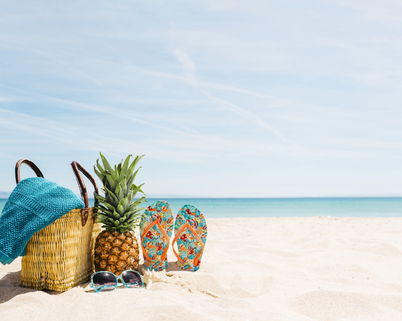 Сумка, ананас, шлепанцы и солнечные очки лежат на песке на пляже летом