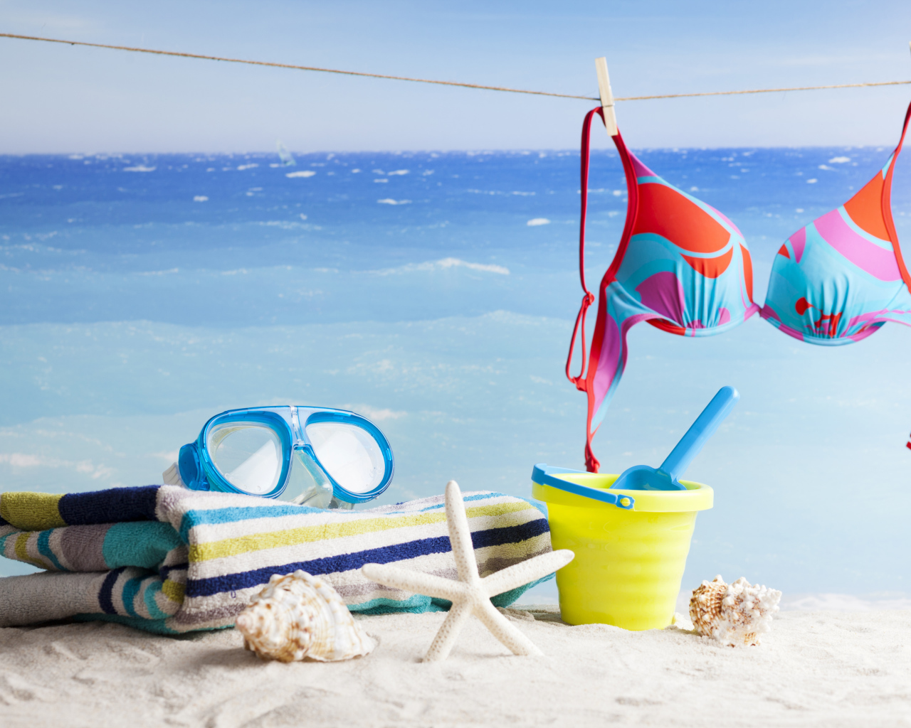 Очки, купальник, полотенце, ракушки и игрушки на песке на пляже летом