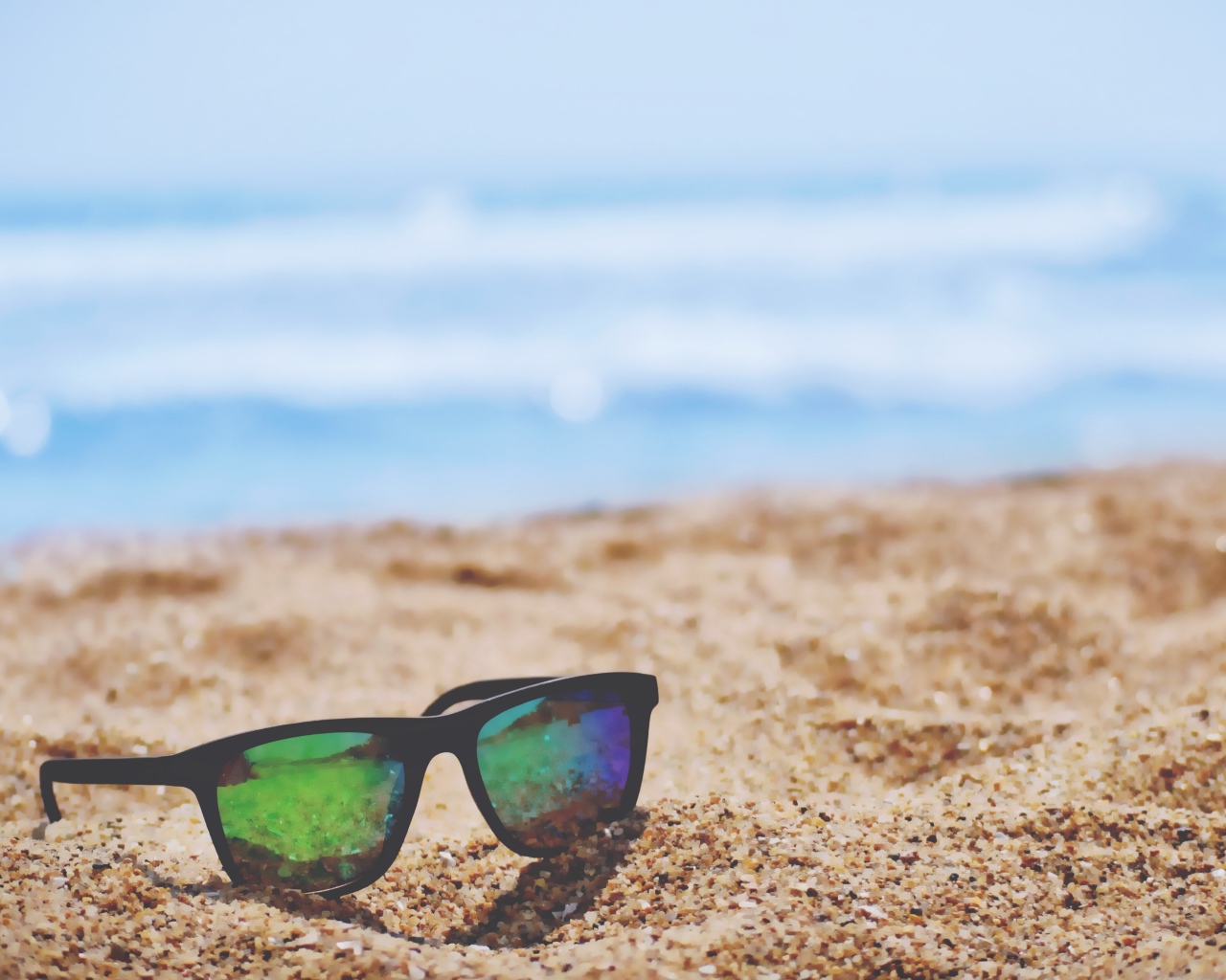 Солнцезащитные очки лежат на желтом песке у моря