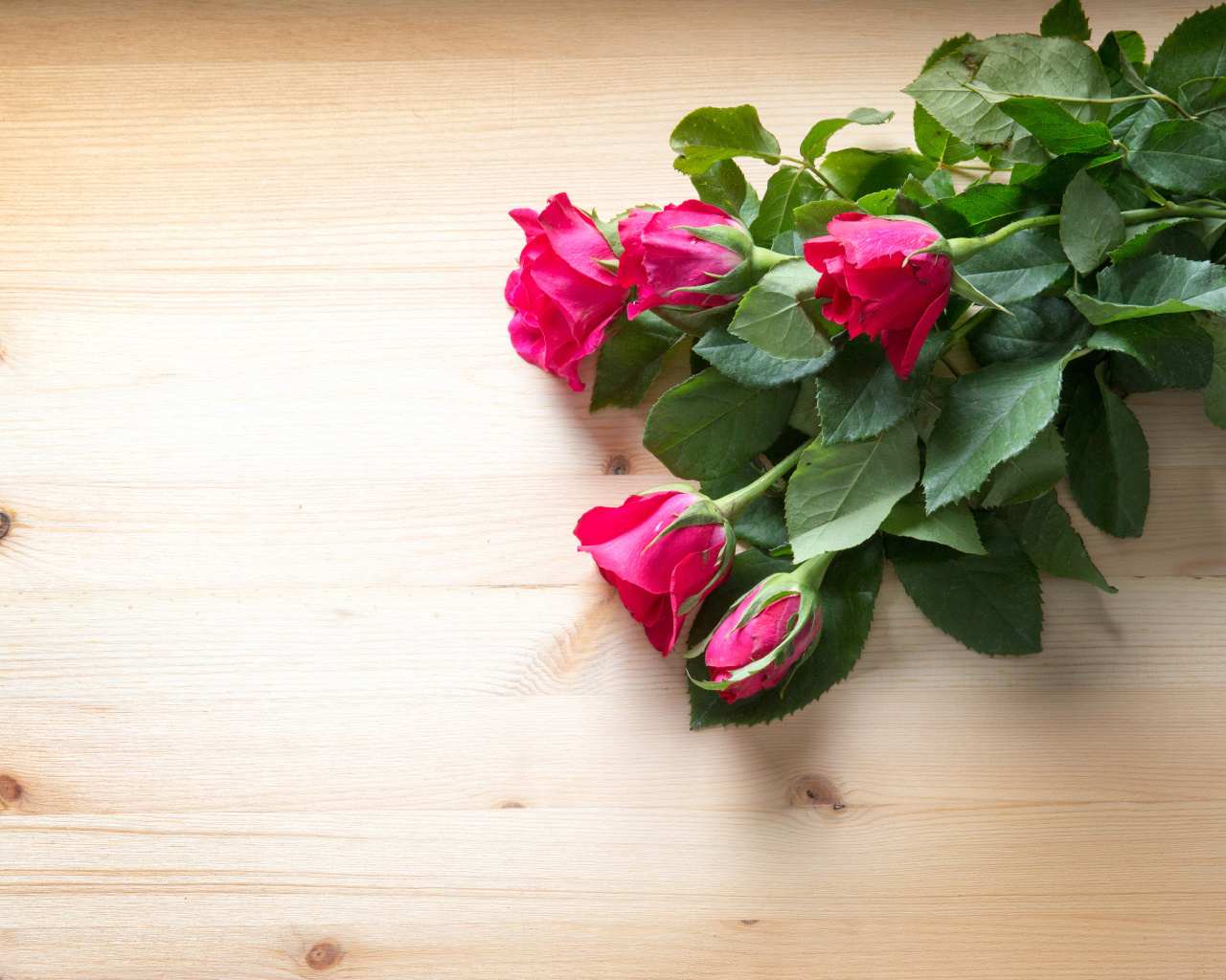 Букет розовых роз с зелеными листьями на деревянной поверхности 